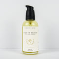 A bottle of Meadows & Myth's 'Tale of Beauty' rose, leather, and sandalwood body oil. The clear bottle shows the pale yellow oil inside, with a cream-colored label and a black pump dispenser, set against a plain white background.