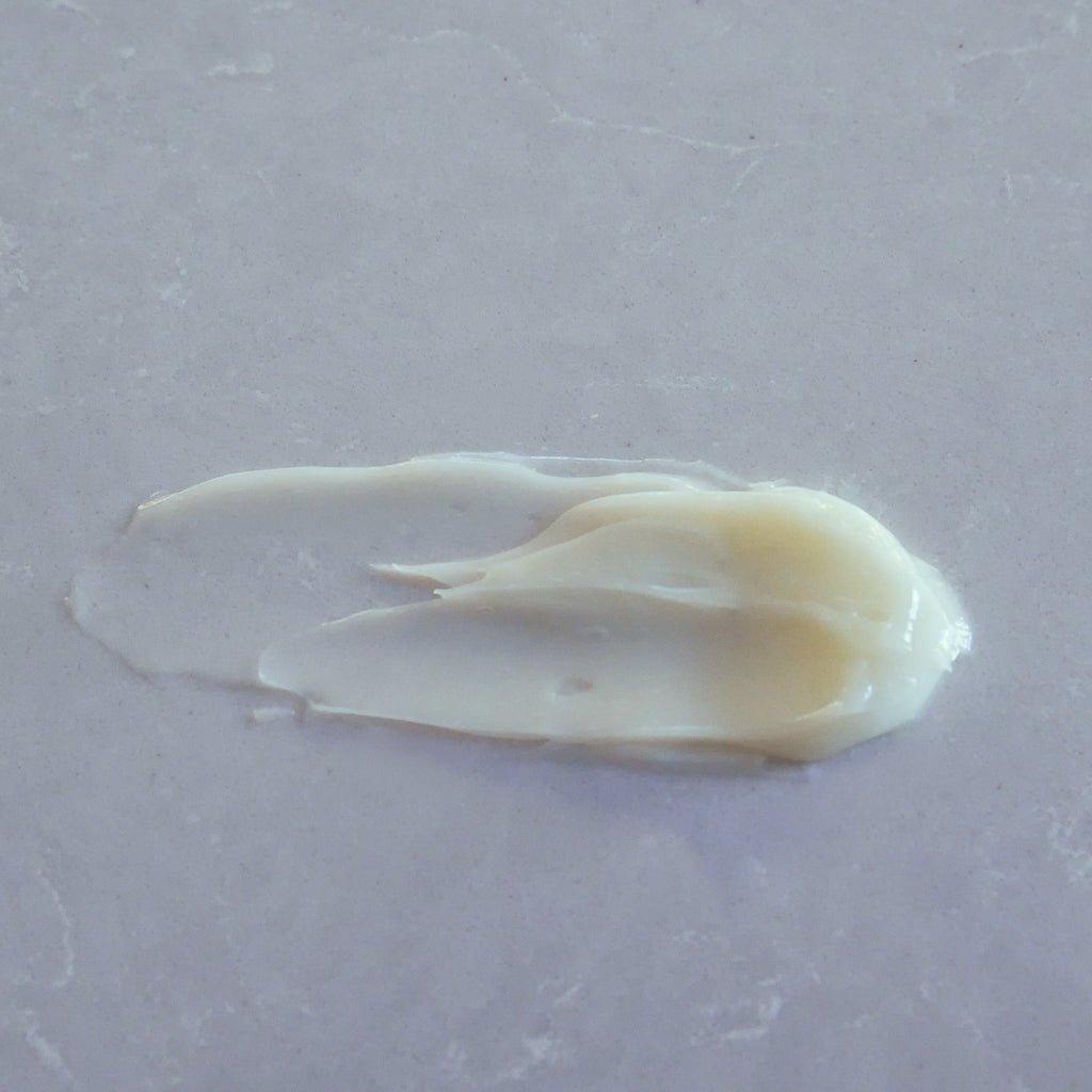 A dollop of creamy off-white body butter spread on a light gray textured surface.
