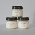 Three jars of Meadows & Myths body butter products stacked in a pyramid on a light gray background. The top jar is 'Glitch' and the bottom two are 'Tale of Beauty' and 'Fae Blossom'.