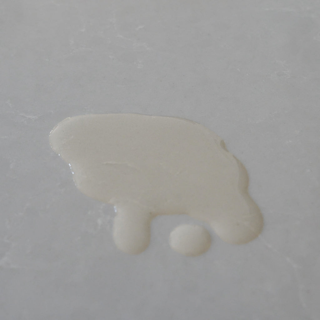 A dollop of creamy light yellow liquid oil on a smooth, light gray surface.
