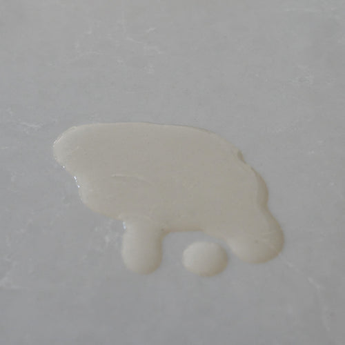 A dollop of creamy light yellow liquid oil on a smooth, light gray surface.