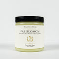 A jar of Meadows & Myth's 'Fae Blossom' velvet body butter, featuring a cream-colored label with gold detailing and a black lid, set against a plain white background.
