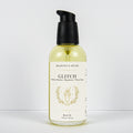 A bottle of Meadows & Myth's Glitch body oil, featuring a clear bottle filled with pale yellow oil, a black pump dispenser, and a cream-colored label with gold text and illustration, set against a plain white background.
