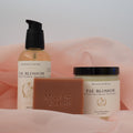 Meadows & Myths 'Fae Blossom' scented body care set featuring a terracotta rectangular soap bar with "Meadows & Myths" embossed on it, a bottle of body oil, and a jar of body butter, sitting on pink fabric with a white background.