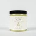 A jar of Meadows & Myth's Oath Velvet Body Butter, featuring a light greenish-yellow balm visible through the clear jar, a cream-colored label with gold text, and a black lid, set against a plain white background.