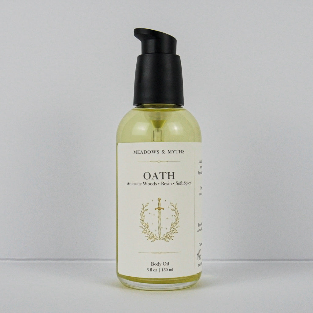 A bottle of Meadows & Myth's Oath Aromatic Woods + Resins + Soft Spots body oil, featuring a black pump dispenser and a cream-colored label with gold detailing, set against a plain light gray background.