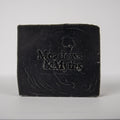 A rectangular bar of dark soap with the brand name 'Meadows & Myths' embossed on the front, set against a plain light gray background.