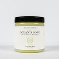 A jar of Meadows & Myth's 'Ocean's Song' velvet body butter, featuring a white label with gold detailing and a black lid, set against a plain white background.