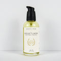 A bottle of Meadows & Myth's 'Ocean's Song' body oil, featuring a clear glass bottle filled with pale yellow oil, a black pump dispenser, and a cream-colored label with gold detailing of a shell, set against a plain white background.