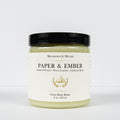 A jar of Meadows & Myth's 'Paper & Ember' velvet body butter, featuring a cream-colored label with gold detailing and a black lid, set against a plain white background.