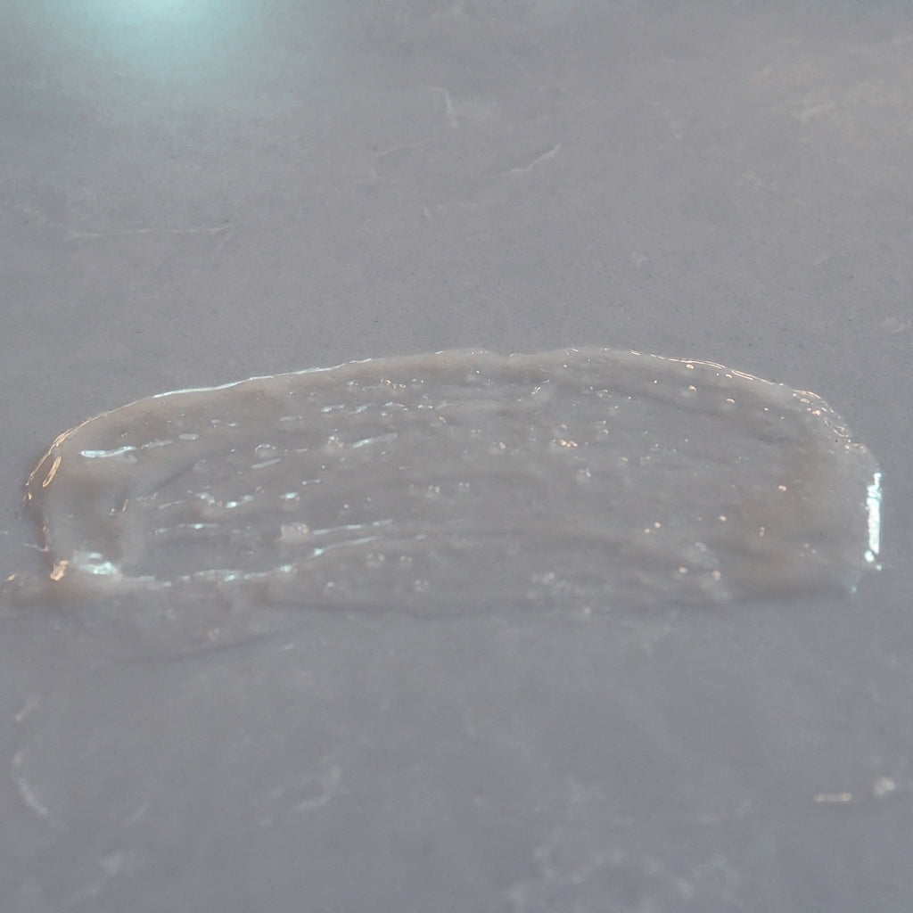 A thick, glossy, white cream sugar scrub smeared horizontally on a matching gray surface.