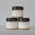 Three jars of Meadows & Myths sugar scrub products stacked in a pyramid on a light gray background. The top jar is 'Fae Blossom' and the bottom two are 'Glitch' and 'Tale of Beauty'.
